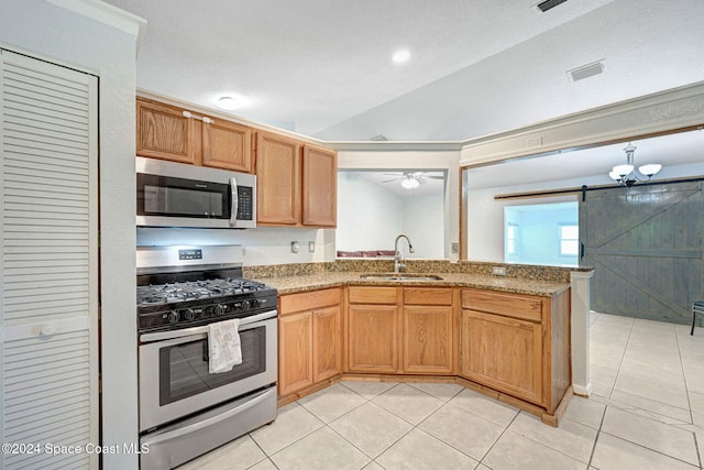 kitchen with lofted ceiling, a barn door, sink, light tile patterned floors, and appliances with stainless steel finishes