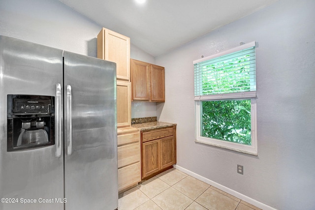 kitchen featuring stainless steel fridge, light tile patterned floors, light stone counters, and vaulted ceiling