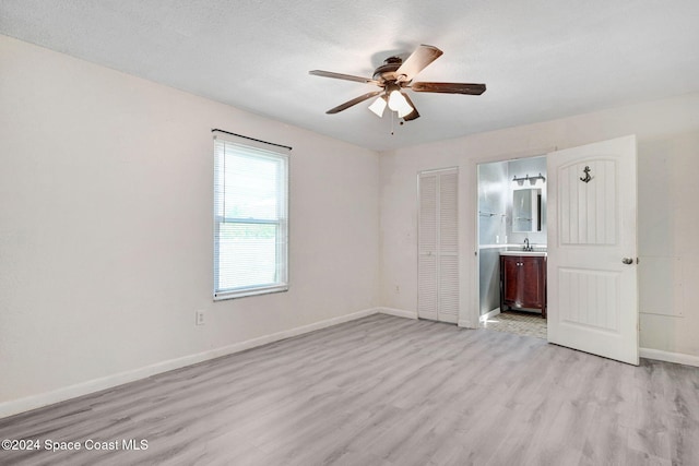 unfurnished bedroom with light hardwood / wood-style floors, a textured ceiling, connected bathroom, ceiling fan, and a closet