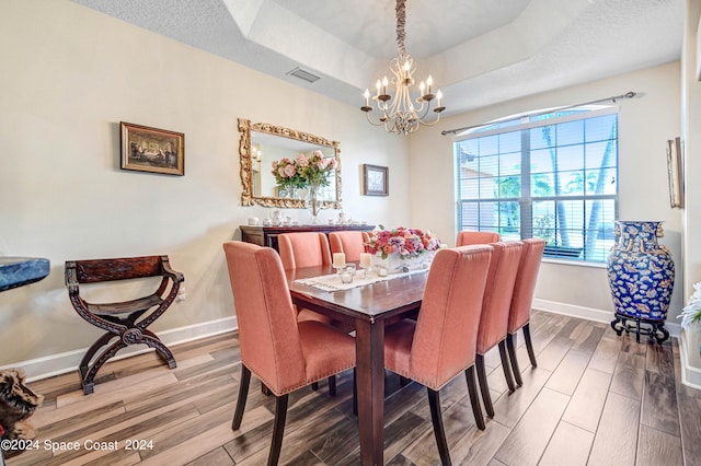 dining area with hardwood / wood-style floors, a notable chandelier, a textured ceiling, and a tray ceiling