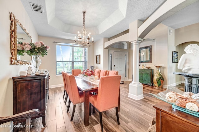 dining room with ornate columns, an inviting chandelier, light hardwood / wood-style floors, a textured ceiling, and a tray ceiling