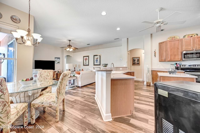 kitchen featuring stainless steel appliances, light hardwood / wood-style floors, sink, ceiling fan with notable chandelier, and hanging light fixtures