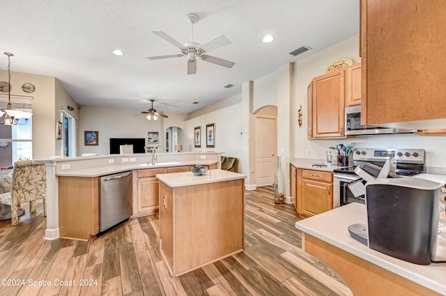 kitchen featuring light hardwood / wood-style floors, ceiling fan, stainless steel appliances, pendant lighting, and a center island with sink