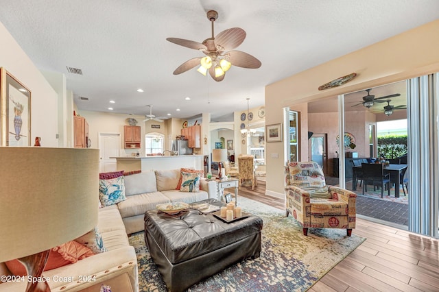 living room featuring ceiling fan, light wood-type flooring, and a textured ceiling