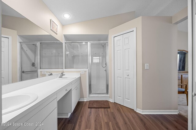 bathroom featuring hardwood / wood-style flooring, a textured ceiling, double vanity, vaulted ceiling, and a shower with door