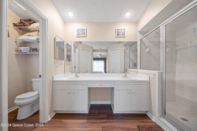 bathroom with hardwood / wood-style flooring, a textured ceiling, dual bowl vanity, toilet, and a shower with door