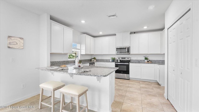 kitchen with a kitchen breakfast bar, light stone countertops, white cabinetry, and stainless steel appliances