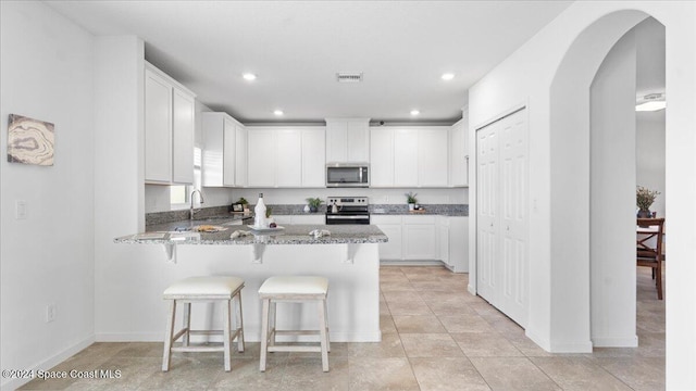 kitchen with white cabinetry, light stone countertops, kitchen peninsula, a breakfast bar, and appliances with stainless steel finishes