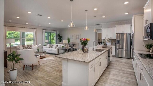 kitchen with appliances with stainless steel finishes, sink, decorative light fixtures, white cabinetry, and an island with sink