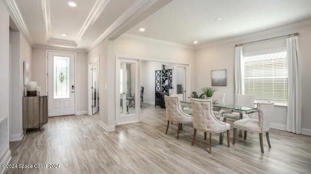 dining room featuring a raised ceiling, ornamental molding, and light wood-type flooring