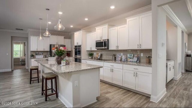 kitchen featuring white cabinetry, hanging light fixtures, stainless steel appliances, decorative backsplash, and a center island with sink