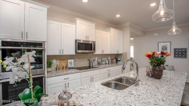 kitchen with appliances with stainless steel finishes, ornamental molding, sink, decorative light fixtures, and white cabinetry