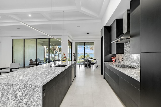 kitchen with wall chimney range hood, coffered ceiling, hanging light fixtures, and backsplash