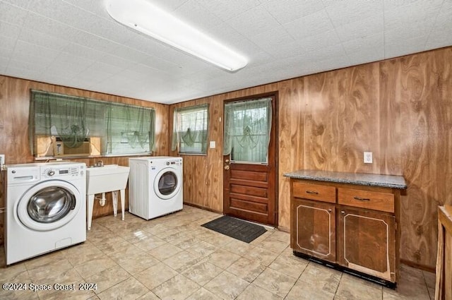 clothes washing area with washer and dryer, cabinets, wood walls, and sink