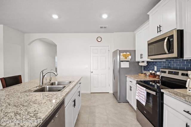 kitchen featuring backsplash, stainless steel appliances, light tile patterned flooring, light stone countertops, and white cabinets