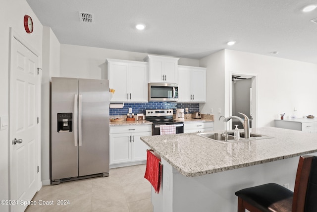 kitchen featuring backsplash, light tile patterned floors, stainless steel appliances, an island with sink, and sink