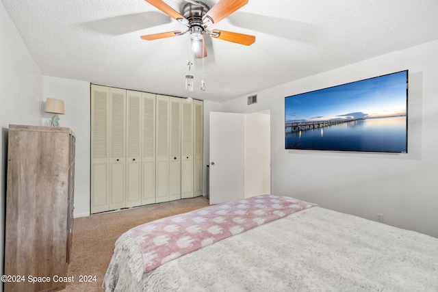 bedroom featuring ceiling fan, a closet, a textured ceiling, and light colored carpet