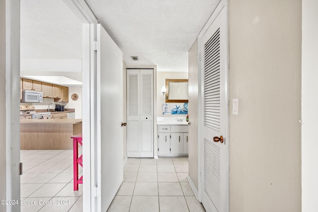 hall featuring sink, a textured ceiling, and light tile patterned flooring