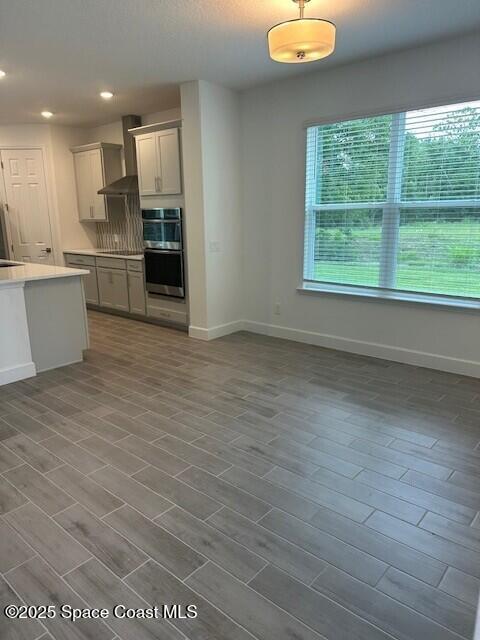 3742 Ornis Ct, Grant-Valkaria, FL 32950 - kitchen with wall chimney range hood, double oven, baseboards, light countertops, and recessed lighting