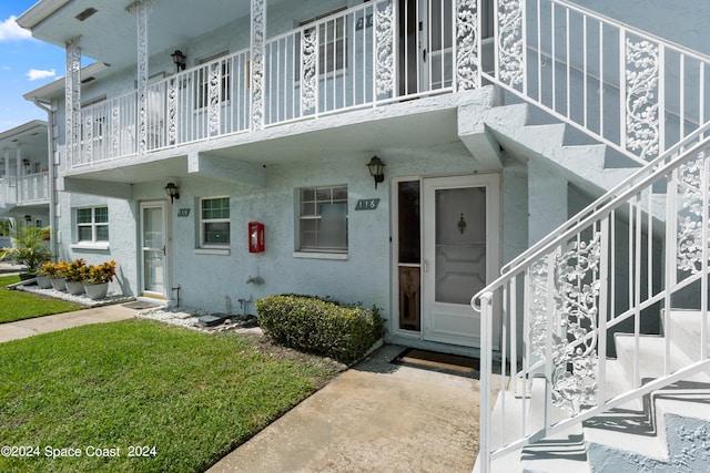 view of exterior entry featuring a yard and a balcony