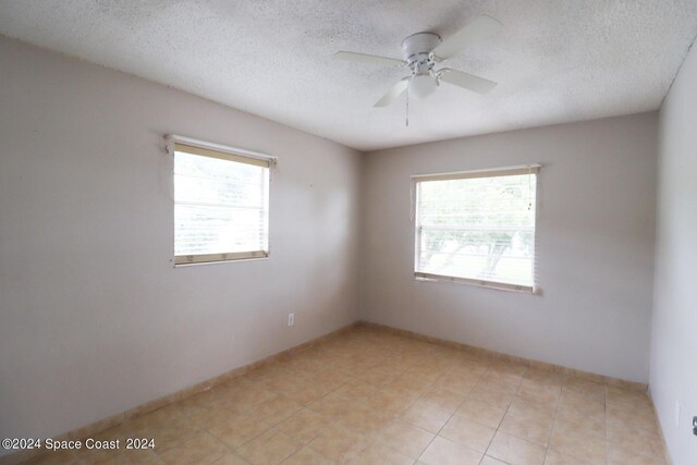 empty room with a textured ceiling, ceiling fan, and light tile patterned flooring