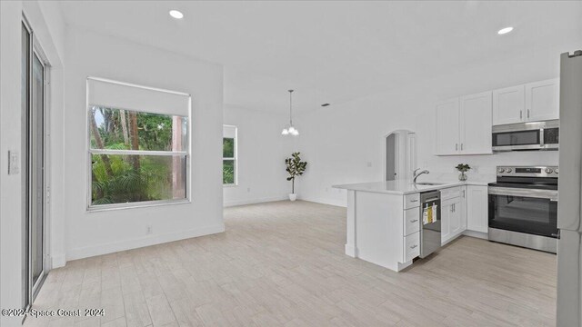 kitchen with white cabinets, light hardwood / wood-style flooring, decorative light fixtures, stainless steel appliances, and kitchen peninsula