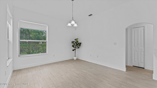 empty room with light wood-type flooring and a notable chandelier