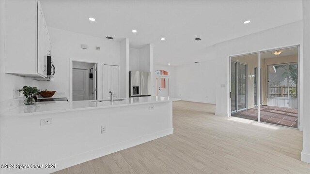 kitchen with stainless steel fridge, white cabinetry, kitchen peninsula, sink, and light hardwood / wood-style floors