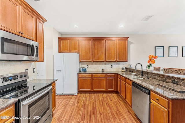 kitchen with stone counters, appliances with stainless steel finishes, light hardwood / wood-style floors, sink, and tasteful backsplash