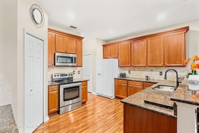 kitchen with dark stone countertops, light hardwood / wood-style flooring, stainless steel appliances, and sink