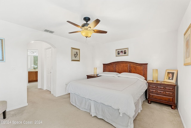 bedroom featuring light colored carpet, ensuite bath, and ceiling fan