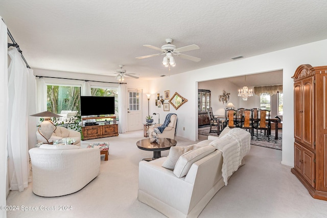 living area with visible vents, light carpet, a textured ceiling, and ceiling fan with notable chandelier