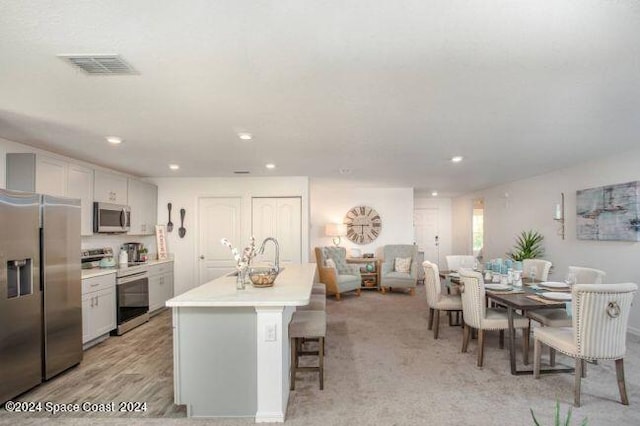 kitchen with light wood-type flooring, a breakfast bar area, an island with sink, white cabinetry, and stainless steel appliances