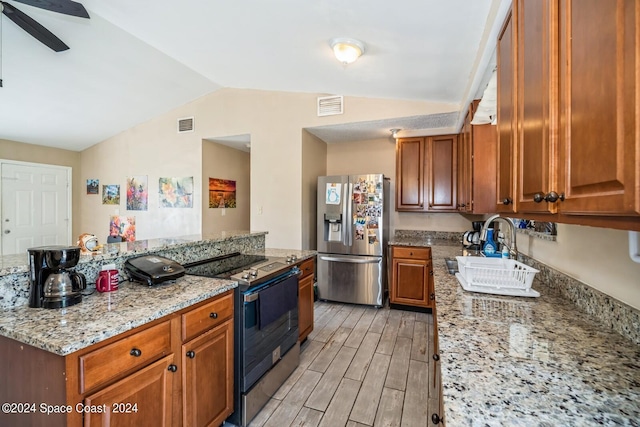 kitchen with light stone counters, stainless steel fridge, sink, light wood-type flooring, and vaulted ceiling