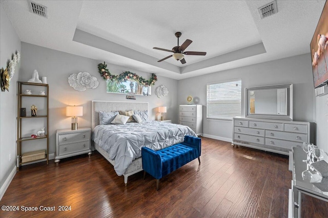 bedroom with a textured ceiling, ceiling fan, a raised ceiling, and dark hardwood / wood-style flooring