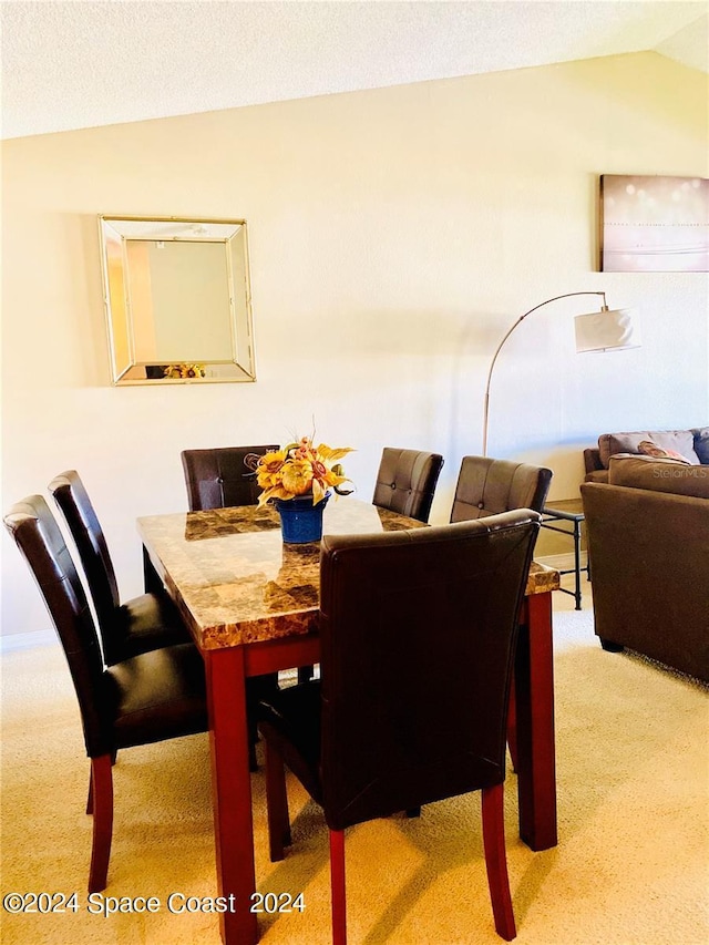 dining space featuring a textured ceiling, vaulted ceiling, and light carpet