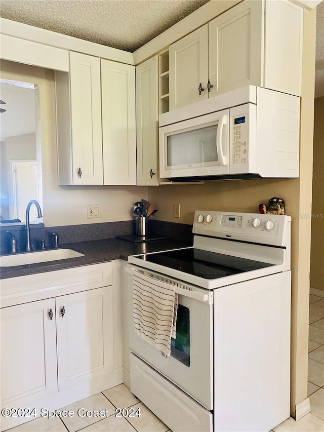 kitchen with white cabinets, sink, a textured ceiling, light tile patterned flooring, and white appliances