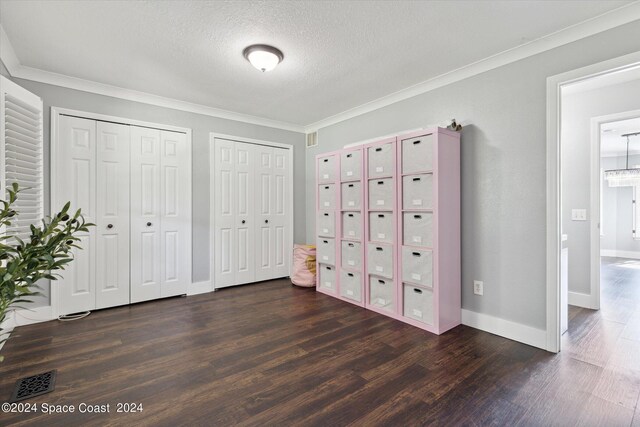 unfurnished bedroom featuring a textured ceiling, dark wood-type flooring, two closets, and crown molding