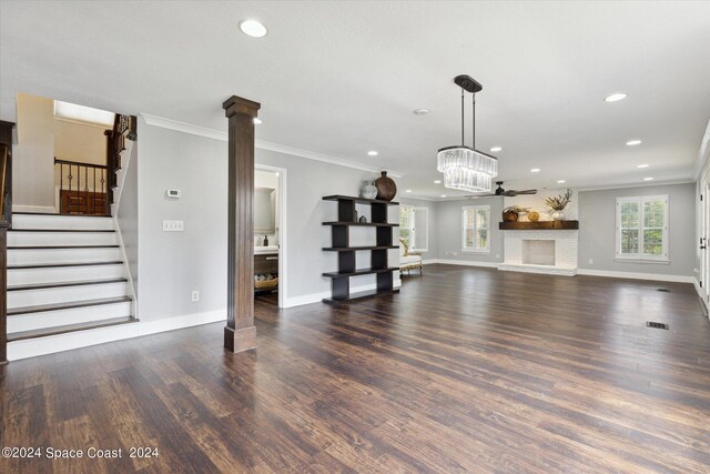 unfurnished living room featuring ceiling fan with notable chandelier, dark hardwood / wood-style floors, ornamental molding, and ornate columns