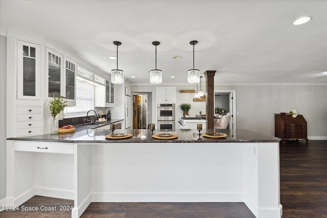 kitchen featuring white cabinetry, kitchen peninsula, stainless steel double oven, dark wood-type flooring, and hanging light fixtures