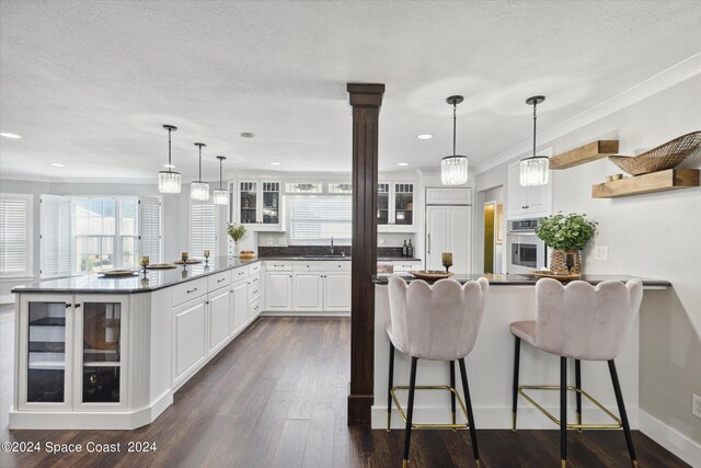 kitchen with a breakfast bar area, pendant lighting, white cabinets, and oven