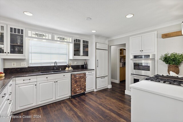 kitchen with appliances with stainless steel finishes, dark wood-type flooring, white cabinetry, sink, and crown molding