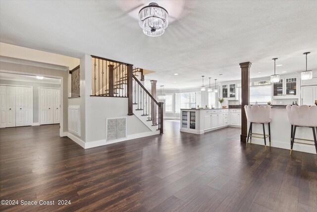 unfurnished living room featuring dark hardwood / wood-style flooring, an inviting chandelier, a textured ceiling, and ornate columns