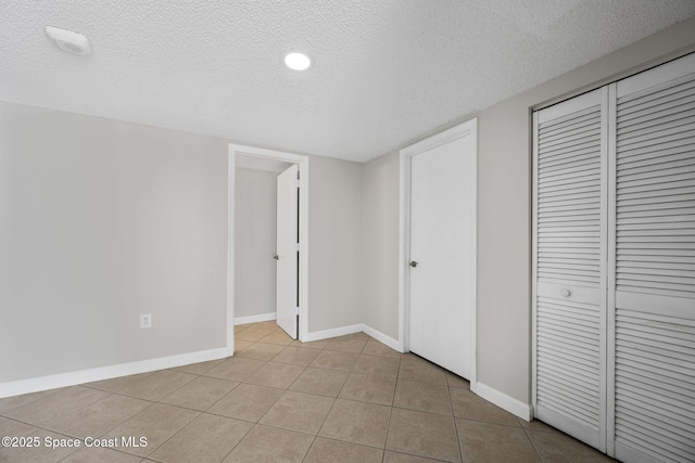 unfurnished bedroom featuring a closet, a textured ceiling, baseboards, and light tile patterned floors