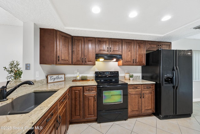 kitchen with light tile patterned floors, light stone counters, under cabinet range hood, black appliances, and a sink