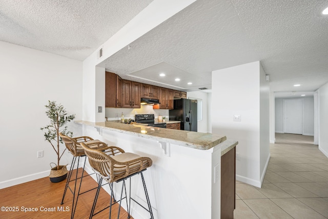 kitchen featuring a kitchen breakfast bar, a peninsula, under cabinet range hood, light countertops, and black appliances