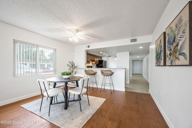 dining room featuring baseboards, ceiling fan, visible vents, and wood finished floors