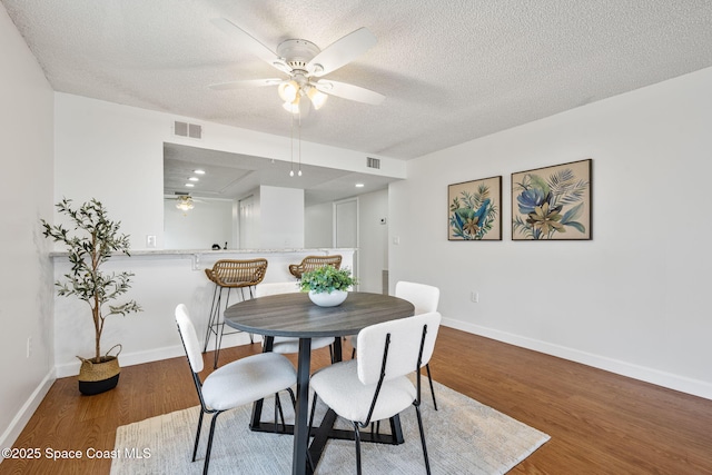 dining room featuring baseboards, a textured ceiling, visible vents, and wood finished floors