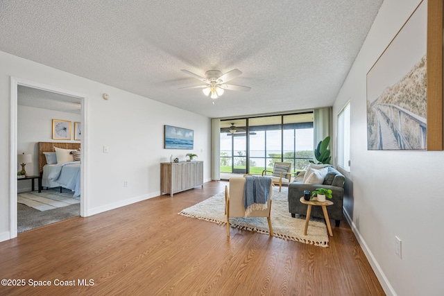 sitting room with baseboards, ceiling fan, wood finished floors, a textured ceiling, and floor to ceiling windows