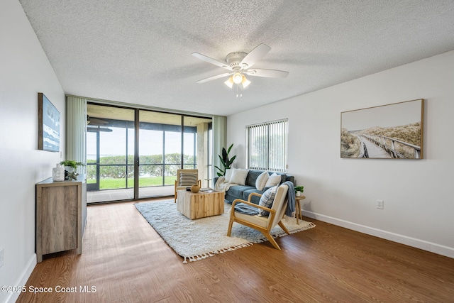 living area featuring baseboards, ceiling fan, wood finished floors, a textured ceiling, and floor to ceiling windows